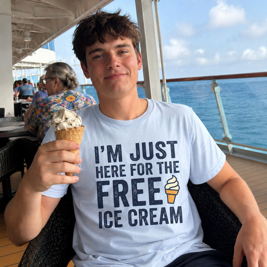 A young man sitting on a cruise ship balcony wearing a light blue graphic t-shirt that reads 'I'M JUST HERE FOR THE FREE ICE CREAM' with a small ice cream cone illustration. He is holding an ice cream cone in his hand, with the ocean and other passengers visible in the background.